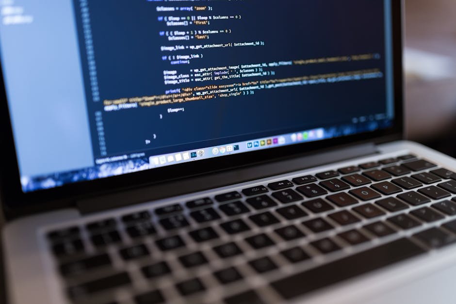 A close-up view of a laptop screen displaying a dark-themed code editor filled with lines of colorful programming code, including syntax highlighting in shades of green, orange, purple, and blue. The 